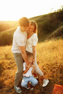 Çok mutlu bir aile sahada yürüyor, gülüyor, neşeli bir anaokulu çocuğu şefkatli bir ailenin, sevgi dolu bir kocanın elini tutuyor sevimli bir eşe sarılıyor, çocukluk ve ebeveynlik kavramı.