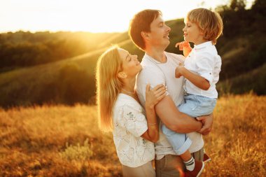 Anaokulunda oğlu olan sevimli ebeveynler sahada yürüyor, ilgili baba neşeli çocuğu kollarına alıyor, gülümsüyor, sevgi dolu anne yakışıklı babayı, ebeveynliği ve çocukluk kavramını nazikçe kucaklıyor.