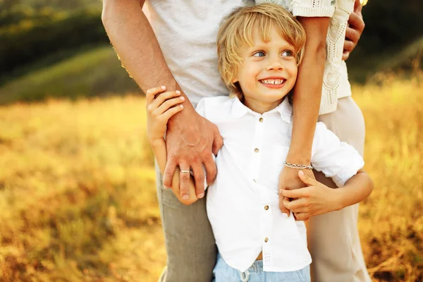 Joyful preschooler boy holding caring parents arms, smiling, happy child with mother and father at the field, family spend time together, childhood and parenthood concept — Stock Photo, Image