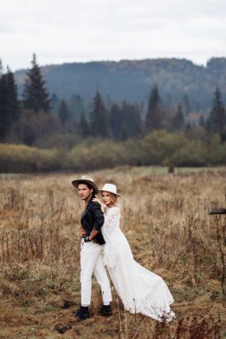 Güzel bir çift sahada poz veriyor, çekici gelin yakışıklı damada sarılıyor, çekici erkek ve güzel kadın kameraya bakıyor, mutlu evliliğin tadını çıkarıyor, düğün fotoshoot konsepti. Yüksek kalite fotoğraf