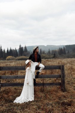 Sahada yürüyen muhteşem bir çift, beyaz dantelli elbise giyen çekici bir kadın, çitte oturan yakışıklı bir adam, güzel bir eş, hafta sonu konsepti. Yüksek kalite fotoğraf