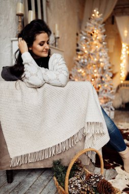 Genç bir kadın Noel ağacıyla aynı odada oturuyor.