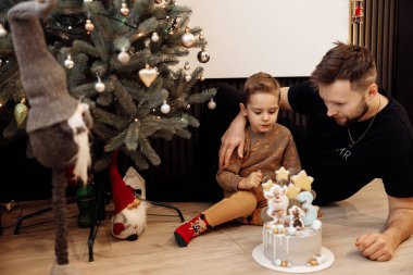 Mutlu baba ve oğul Noel ağacının yanında pastayla 