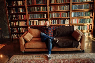 Genç adam kütüphanede kanepede oturuyor. 