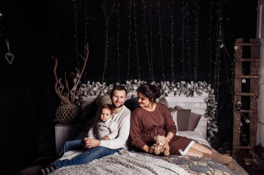 Mutlu bir aile yatakta oğluyla oturuyor. 