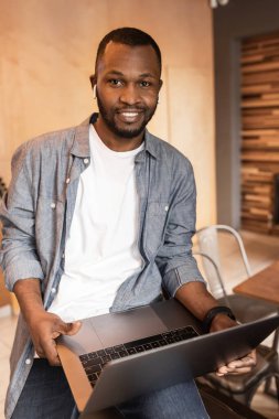 Yakışıklı genç adam masada oturuyor ve dizüstü bilgisayar kullanıyor. 