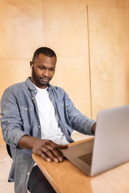 Yakışıklı genç adam masada oturuyor ve dizüstü bilgisayar kullanıyor. 