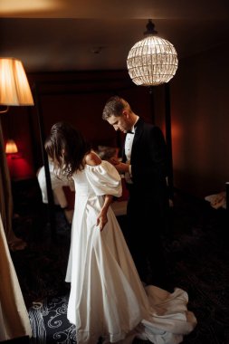 Mutlu genç damat gelinin giyinmesine yardım ediyor.