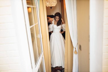 Mutlu genç damat gelinin giyinmesine yardım ediyor.