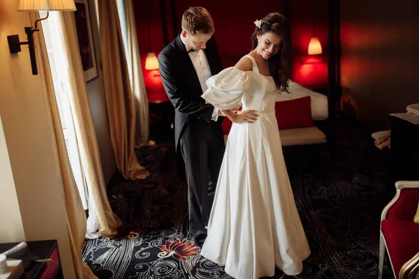 幸せな若い新郎は花嫁がドレスを着るのを助ける — ストック写真