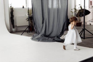 Beyaz elbiseli küçük kız stüdyoda poz veriyor.