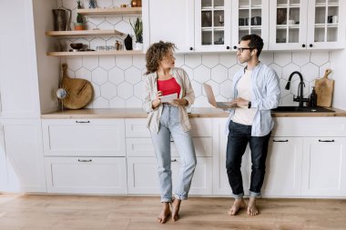 Genç çift evdeki mutfakta dizüstü bilgisayar kullanıyor. 