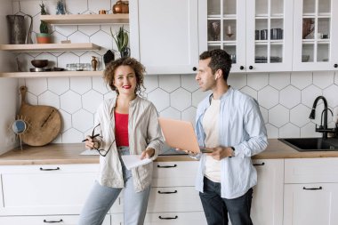 Genç çift evdeki mutfakta dizüstü bilgisayar kullanıyor. 