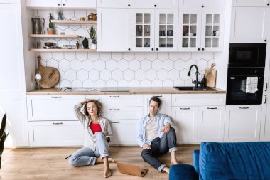 Genç çift evdeki mutfakta dizüstü bilgisayar kullanıyor. 