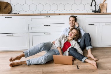 Genç çift evdeki mutfakta dizüstü bilgisayar kullanıyor. 