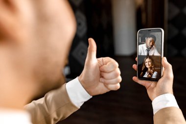 Akıllı telefonlu bir işadamı baş parmağını gösteriyor. 