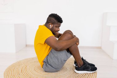 Afro-Amerikan bir adam yerde oturuyor ve başka tarafa bakıyor. 