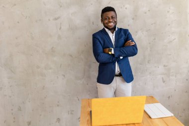 Takım elbiseli ve ceketli yakışıklı Afro-Amerikan işadamı kameraya bakıyor ve gülümsüyor.