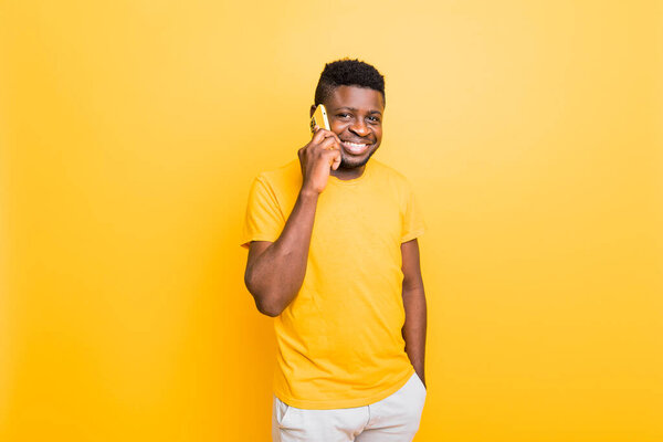 Young african american man with a mobile phone on yellow background