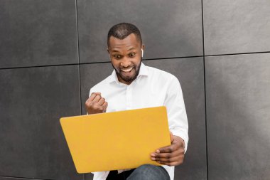 Sokakta dizüstü bilgisayar kullanan beyaz gömlekli mutlu bir Afro-Amerikan.