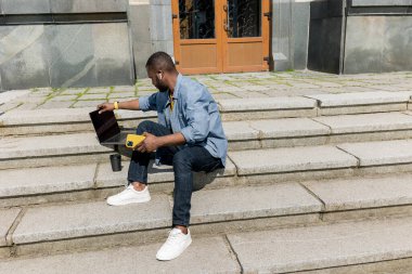 Dizüstü bilgisayarı olan ve merdivenlerde oturan genç yakışıklı adam. 