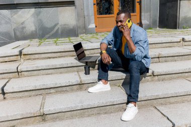 Dizüstü bilgisayarı olan ve merdivenlerde oturan genç yakışıklı adam. 