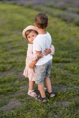 Küçük çocuk ve kız çiçeklerle dolu bir alanda eğleniyorlar.