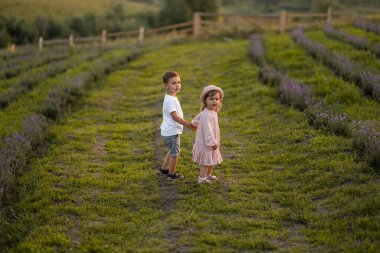 Küçük çocuk ve kız çiçeklerle dolu bir alanda eğleniyorlar.