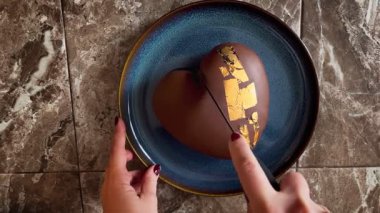 Bir el, Sevgililer Günü 'nü kutlamak için mavi bir tabakta zengin bir çikolata kalbini dikkatlice keser. Sıcak bir atmosferde tatlı ikramının tadını çıkar.