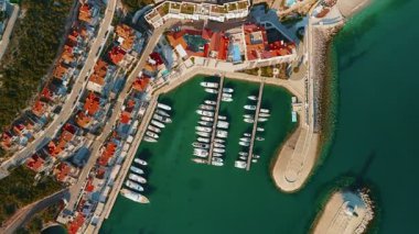 Akdeniz 'de bir kasabada, öğleden sonra güneşlenirken, havadan bakıldığında parmak iskeleleri, demirli yatlar, kıvrımlı dalgakıranlar ve yuvarlak iskele başı görülüyor..