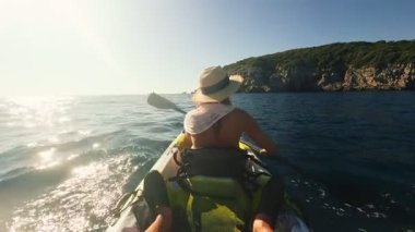 Sarı kanonun arkasındaki POV 'a göre saman şapkalı kadın sert kireçtaşı kıyılarına doğru kürek çekiyor, düşük güneş ışığı, köpüklü uyanış, lensler, geniş açı..