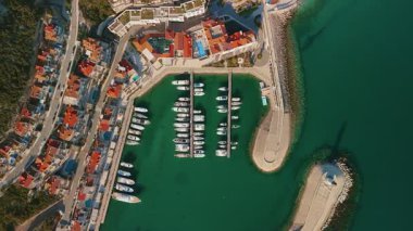 Havadan bakıldığında, parmak rıhtımlarında yatları, palmiye şekilli gezinti alanları, kıvrımlı dalgalar, küçük deniz feneri, turuncu çatılar ve sakin suları olan Karadağ marinası görülüyor.