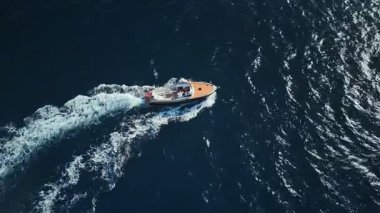 Hava görüntüsü, Karadağ yakınlarındaki derin mavi Adriyatik sularında seyreden küçük bir ahşap motorlu tekne gösteriyor. Köpüklü ikizler güneş ışığı altında iz sürüyorlar ve bir teknede yeni evlenmişler.