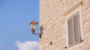 Kameranın fenerden kepenklere doğru döndüğü Karadağ 'da güneş ışığıyla aydınlanan bal renkli taş cephe kireç taşı dokusu, metal kancalar ve menteşeleri ortaya çıkarıyor.