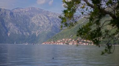 Kotor Körfezi, kilise çan kulesi, sakin su, yelkenli ve motorlu tekne, dik kireçtaşı yamaçlar, doğal ışık, geniş manzara.