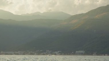 Adriyatik 'in sakin sularına doğru uzanan beton bir iskele, Karadağ' ın kıyı kasabasına doğru uzanırken, güneşli dağlar, küçük botlar ve altın saatinde parıldayan spreyle.