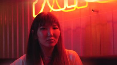 Genç ve güzel bir Asyalı kadının portresi neon ışıkların arka planında. Asya mutfağı olan fast food restoranı. Neon hiyeroglifli büyük kırmızı işaret..