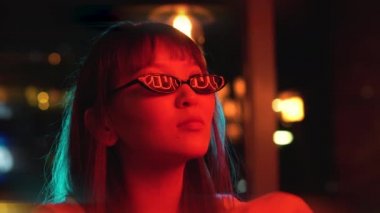 Genç ve güzel bir Asyalı kadının portresi neon ışıkların arka planında. Güneş gözlüklerindeki neon hiyerogliflerin yansıması.