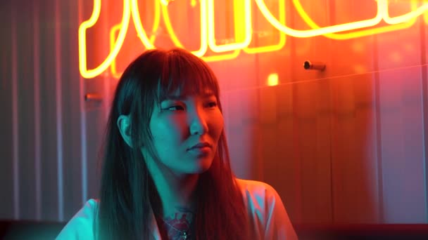 一个年轻美丽的亚洲女人在霓虹灯背景下的画像 有亚洲菜的快餐馆 带有霓虹灯象形文字的大红色标志 — 图库视频影像