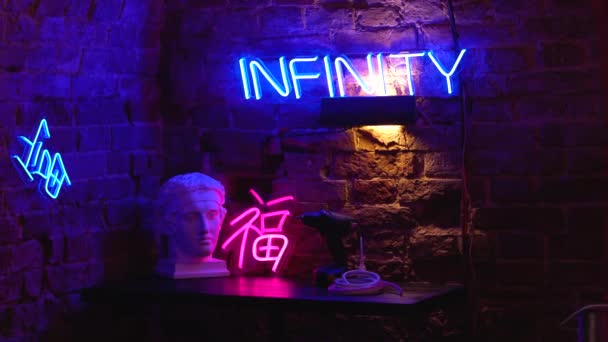 Neonowe znaki w pracowni artystycznej obok głowicy tynku. Jasne kolory z różowymi i niebieskimi pasemkami na stole w studiu ultrafioletowym. — Wideo stockowe