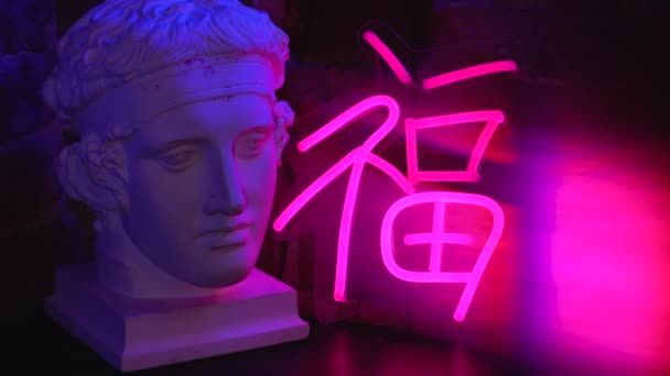 Neon skyltar i konstnärsateljén bredvid gipshuvudet. Ljusa färger med rosa och blå slingor på ett bord i en ultraviolett studio. — Stockvideo