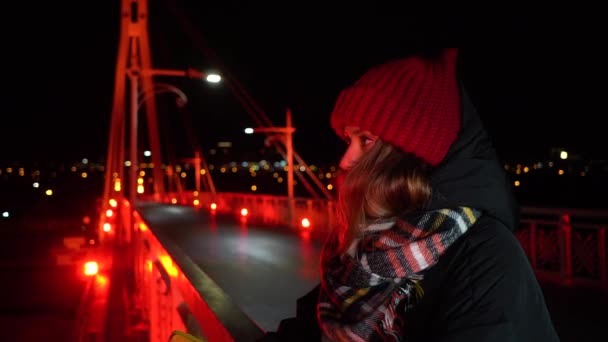 輝く橋の上で暖かい服を着て夜にポーズを若い美しい女の子 ネオン橋の近代的な都市 Tyumen ロシアでは赤で点灯 クローズアップ 4Kビデオ — ストック動画