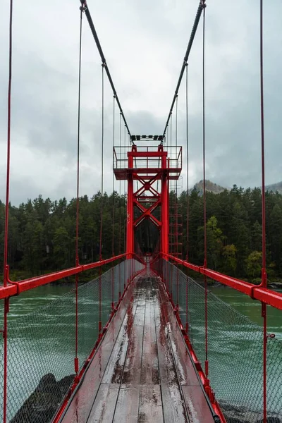 High arched red bridge over the river in the forest.