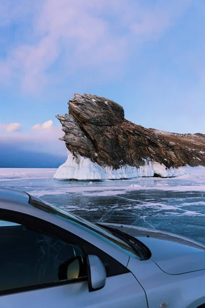 Ogoy isla en el lago Baikal en invierno. Un coche gris se levanta sobre hielo claro contra el telón de fondo de una hermosa roca. Fotos de stock