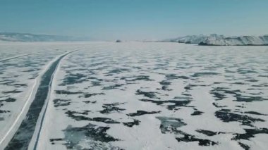 Donmuş Baykal Gölü, adaya giden buz geçidi. Buzlu arabaya giden yol. Turkuaz, çatlaklı berrak buz karla kaplı. Güzel kış manzarası, hava manzarası. 4K video, 60 fps.