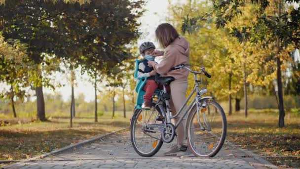 Mam zet een medisch masker op aan kleine zoon voor het fietsen — Stockvideo