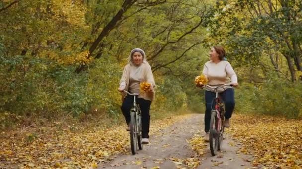 Mulheres idosas felizes gostam de andar de bicicleta no parque de outono — Vídeo de Stock