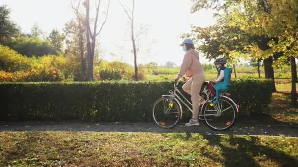 Mamma och son bär medicinska masker cykla i parken — Stockvideo