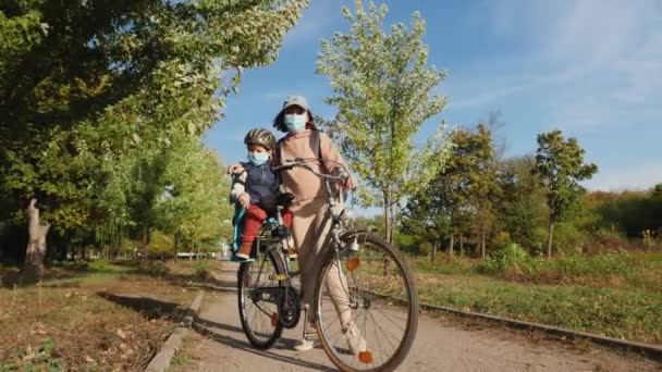 Mãe com seu filho em máscaras e com uma bicicleta no parque — Vídeo de Stock
