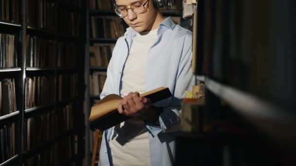 Um adolescente em uma biblioteca lê um livro — Vídeo de Stock